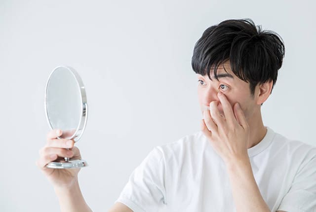 目元を指で抑え、手鏡で見る男性